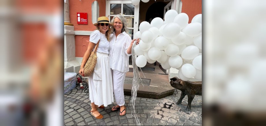 Dämmershoppen Das Bild zeigt zwei Personen vor dem Rathaus während der Veranstaltung Dämmershoppen mit weißen Luftballons.