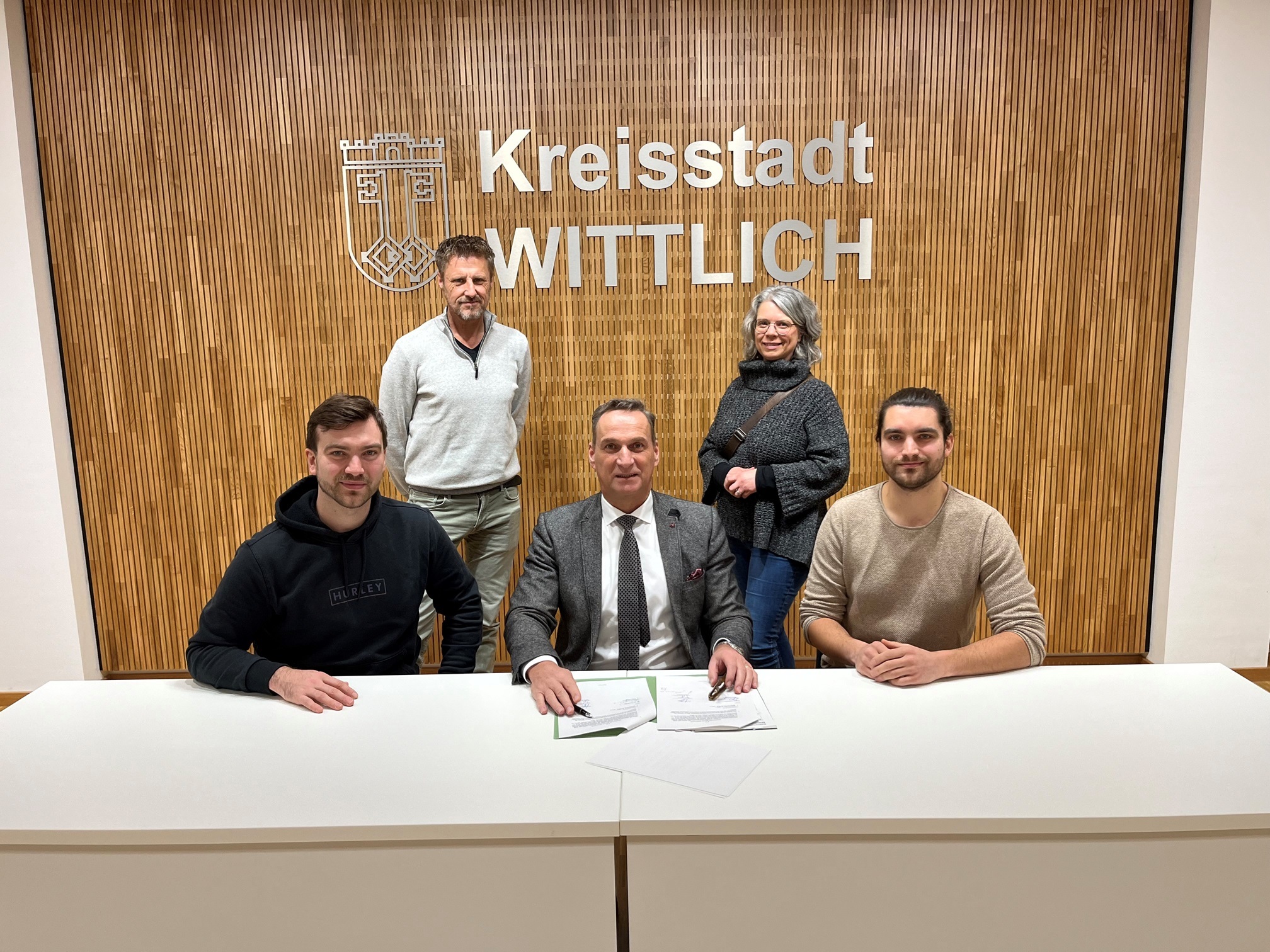 Bürgermeister Joachim Rodenkirch und die beide Brüder Niklas und Jonas Butzen unterzeichnen den Pachtvertrag für den Wohnmobilstellplatz Zweibächen in Wittlich. Bei der Unterzeichnung waren der Fachbereichsleiter Rainer Wener (hinten stehend links) und die Leiterin der Tourist-Information Wittlich Nicole Baller mit dabei (Foto: Sebastian Klein.)