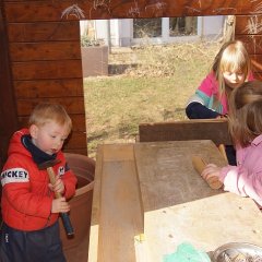 Drei Kinder stehen an der Werkbank, der Junge hat einen Hammer in der Hand und hämmert gegen den Holztisch, zwei Mädchen sägen gemeinsam ein Stück Holz mit der Säge