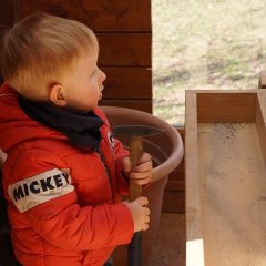 Der Junge mit dem Hammer schaut den Mädchen zu, dabei hält er einen Hammer in der Hand.