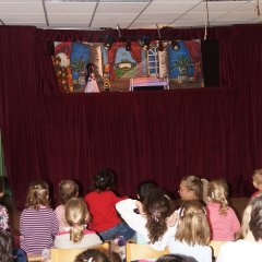 Die Kinder und Erzieher sitzen vor der Bühne und schauen der Prinzessin im Theaterstück zu. 