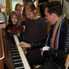 Ein Mitarbeiter der Harzer Puppenbühne spielt Klavier. Um ihn rum stehen viele begeistere Kinder. 
