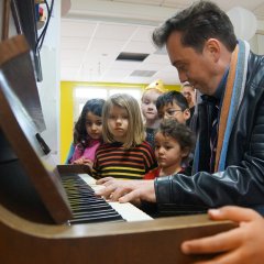 Ein Mitarbeiter der Harzer Puppenbühne spielt auf dem Klavier, um ihn herum stehen viele begeisterte Kinder. 