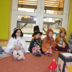 Auf dem Bild sieh man Kinder im Kreis sitzen. Ein paar Kinder sind als Prinzessin, Engel, Tiger, Löwe und Hund verkleidet und schauen zur Erzieherin. In der Mitte steht eine selbstgebastelte Laterne und ein Pferd mit einer Figur die einen roten Umhang und einen Helm trägt. 