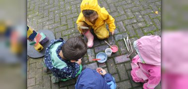 Auf dem Bild sitzen Kinder Draußen und malen mit Kreidefarbe auf Steine.