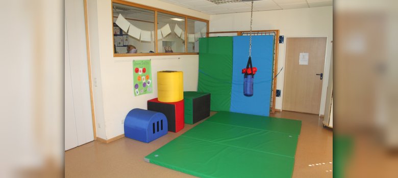 Bewegungsraum Auf dem Bild ist der Bewegungsraum. In der Mitte vom Raum liegen Matten und darüber hängt ein Kinderboxsack. An der Wand sind weitere Matten.