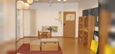 Wiesengruppe Auf dem Bild sieht man die Wiesengruppe. Es steht ein Spielpodest in der Mitte des Raumes. An der Wand hängen mehrere Spielmöglichkeiten und ein Schrank mit Spielmaterial ist zu sehen.