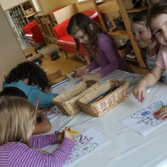 5 Kinder sitzen am Tisch und malen Schmetterlinge mit Wasserfarben aus. 