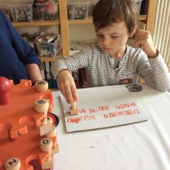 Ein Kind sitzt am Tisch und stempelt mit Buchstaben ein Kinderrecht auf Pappkarton.