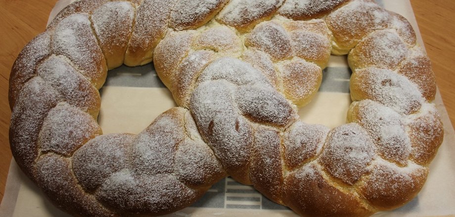 Das Bild zeigt eine riesige geflochtene Martinsbrezel mit Zucker auf einem Tisch.