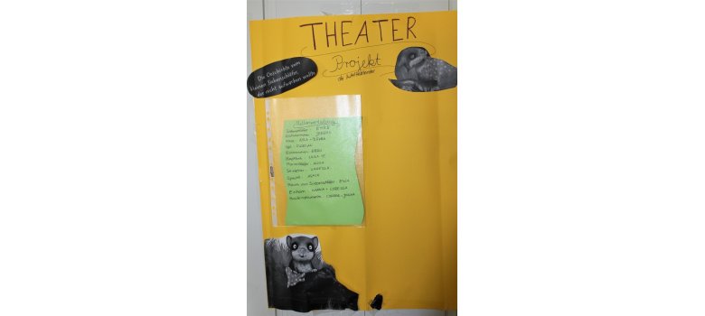 Auf dem Bild ist ein gelber Plakat zu sehen mit dem Titel "Theater Projekt der Mittelfeldkinder" ganz oben. Auf schwarzem Tonkarton steht am Rande "Die Geschichte vom kleinen Siebenschläfer, der nicht aufwachen wollte". In einer Klarsichtfolie steckt ein grünes Blatt Papier auf dem steht die Rollenverteilung der Kinder im Theaterstück. Oben und unten in der Ecke ist ein schwarzweiß Foto des Siebenschläfers.