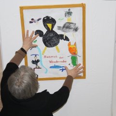 Das Bild zeigt Frau Münzel aus der Stadtbücherei die das Gemälde des Raben Rasmus an die Wand hängt.