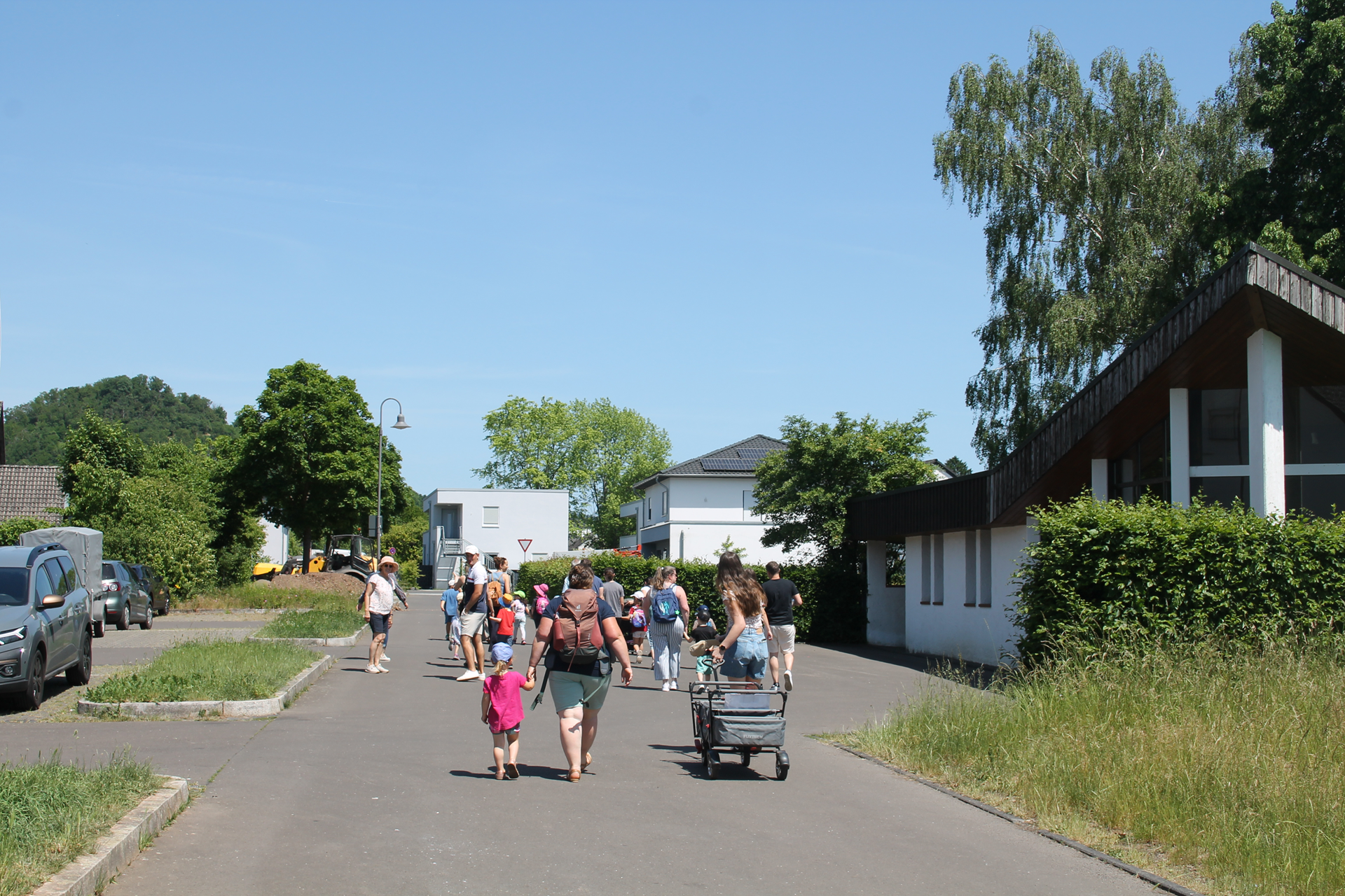 Auf dem Bild ist eine Gruppe von Eltern und Kindern mit Erzieher/innen zu sehen. Sie gehen durch das Dorf.