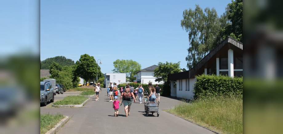 Auf dem Bild ist eine Gruppe von Eltern und Kindern mit Erzieher/innen zu sehen. Sie gehen durch das Dorf.